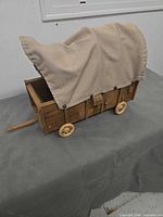 Left-front view showing wood body, canvas cover, wheels, pull tongue