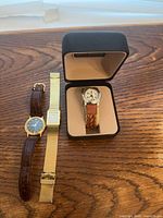 Three wristwatches and watch box on wooden surface