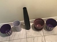 Five containers lined up: two metal buckets, one lavender metal vase, mauve ceramic pot, tall glass vase