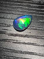 Pear-shaped opal showing strong green and yellow play-of-color on dark background