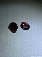 Two round faceted red gemstones on grey surface