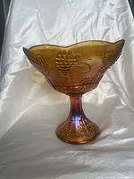 Side view of amber carnival glass pedestal compote showing grapes and leaves pattern