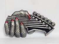Front view of silver-tone belt buckle showing scaly hand, guitar headstock, red enamel accents and skull tuning pegs