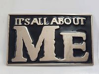 Front view showing ITS ALL ABOUT ME lettering, black enamel, silver-tone finish