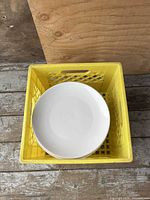 Top view of stack of white dinner plates inside yellow crate