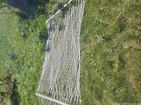 Full view of rope hammock laid on grass showing net and both spreader bars