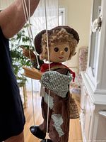 Full view of marionette suspended by strings, showing face, clothing, and tag