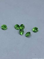 Six vivid green round-cut tsavorite garnets on neutral background