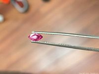 Side profile of marquise ruby held in tweezers showing thickness and clarity
