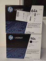 Front view of both HP toner cartridge boxes stacked, showing models 64A and 90A