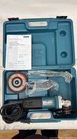 Open case showing angle grinder, wheel, handle, wrench, manual