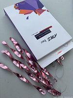 Retail box labeled Ams Inc with several metallic pink spiral icicle ornaments visible, showing design, color and included hanging cords