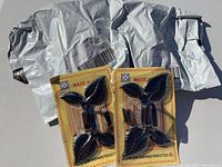 Two visible blister packs of black leaf wall hooks on printed cards; two grey shipping bags indicating third unopened pack