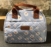 Front view of quilted daisy print lunch bag showing handles and brand patch