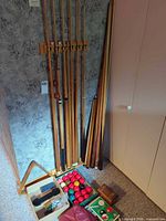 Overall view of cue rack with cues, additional cues, triangle rack, ball set and accessories on floor