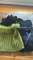 Three sweaters and scarf laid out: green fur-trim strapless knit, black ruffled scarf, black lace-up sweater