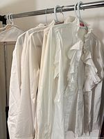Rack view showing several white blouses with ruffle fronts on hangers