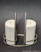 Front view of two white ceramic shakers seated in metal caddy