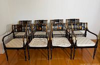 Full front view of all eight black and gilt chinoiserie armchairs with cream cushions