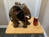 Front and side view of carved wooden elephant beside soda can for scale