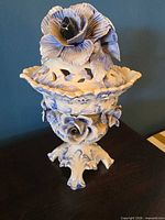 Full view of porcelain compote urn with lid showing applied flowers and pedestal base