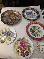 Seven decorative plates and pin dish displayed face up showing patterns and sizes