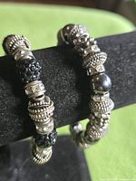 Two silver-tone stretch charm bracelets on display bar