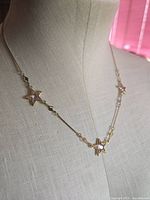 Necklace draped on bust showing left star pendant with pink centre and chain links