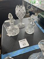 Three clear glass items: pedestal vase and two cruets with stoppers