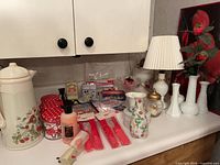 Countertop view showing ceramic canister, polka-dot lid jars, milk glass vases, pitcher, red utensil sets and assorted small decor