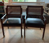 Front view of both armchairs showing cane backs, wood frames, vinyl seats, casters