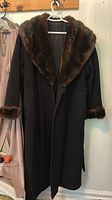 Front view of black wool coat with brown fur collar and cuffs on hanger