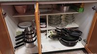 Overview of cabinet showing stacked saucepans, frying pans, plates, casserole dishes