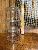 full view of three clear glass stacking canisters assembled with lid beside ruler for scale