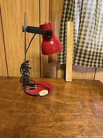 Side view of red metal adjustable desk lamp next to ruler showing height at about 12 inches, cord and inline switch visible
