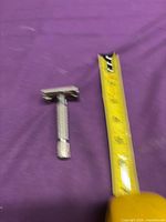 Full view of chrome safety razor beside tape measure