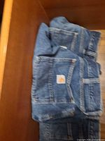 Three folded Carhartt blue jeans with logo patch visible on back pockets