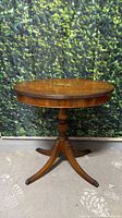 Full view of round honey veneer pedestal side table with painted medallion top and four splayed legs