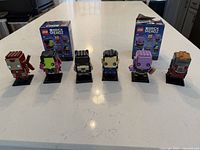 Front view of six assembled BrickHeadz figures with two boxes behind