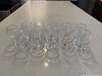 Front view of 11 clear small brandy snifter glasses lined on countertop