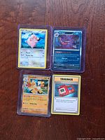All four Pokémon cards in sleeves on wood surface