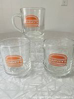 Three Harvey's glass mugs on table, logo visible