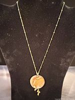 Full view of Lia Sophia gold-tone chain and round abalone pendant with dangling drops