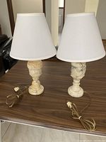 Both marble/alabaster lamps with shades and cords on tabletop