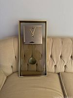 Front view of Labar gold/brass pendulum wall clock on sofa