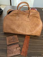 Overall view of tan leather duffel with three leather accessories
