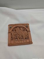 Front of terracotta plaque with owl and winter scene, "Winter" text visible