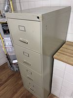 Front left view of beige 4-drawer metal filing cabinet showing label holders and missing lock