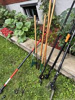 Group of long-handled garden tools leaning against stone border
