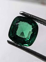 Front view of cushion-cut green gemstone held in tweezers